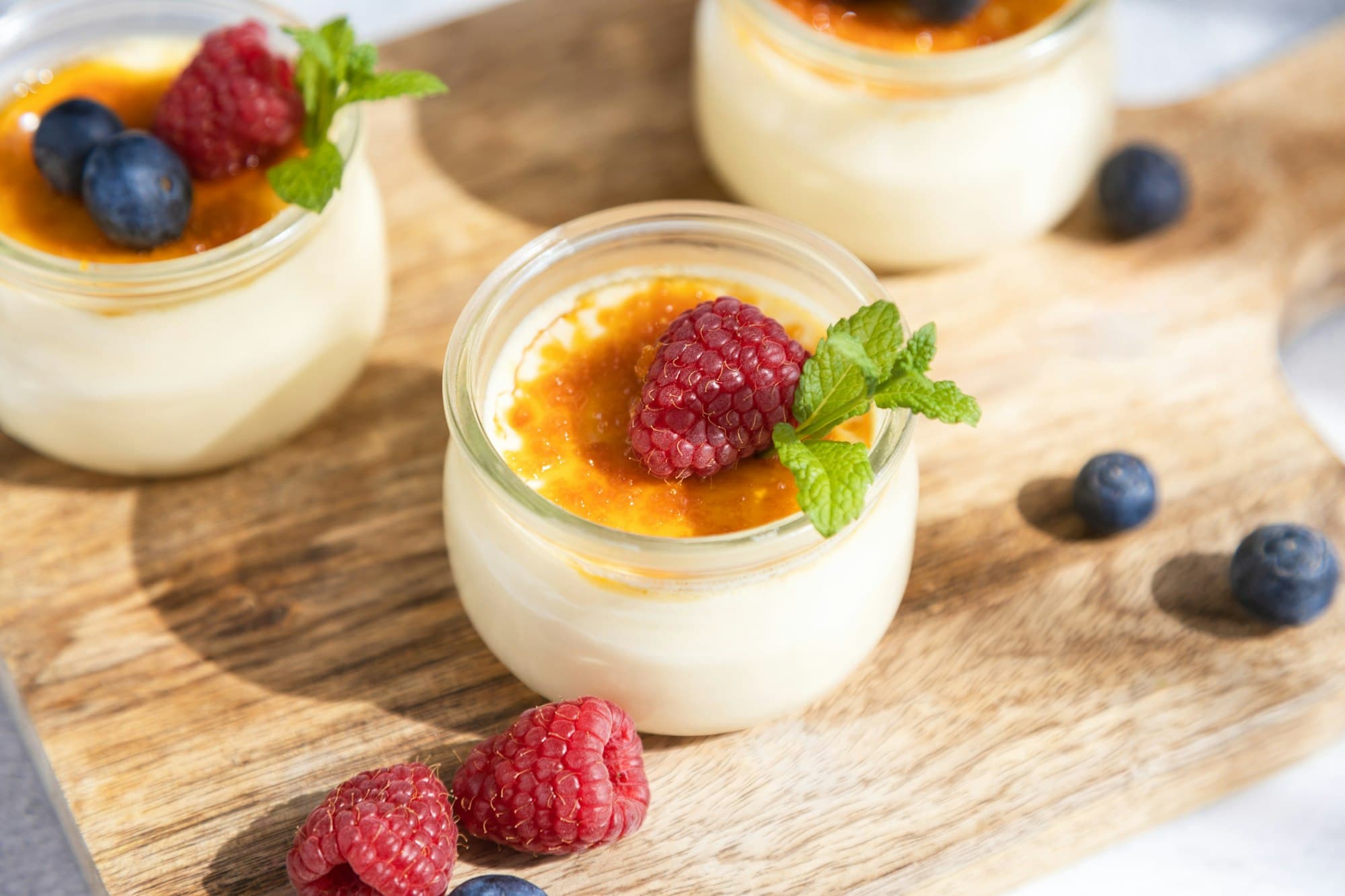 Close-up of a creme brulee dessert garnished with fresh sprig of mint and berries on a cutting board